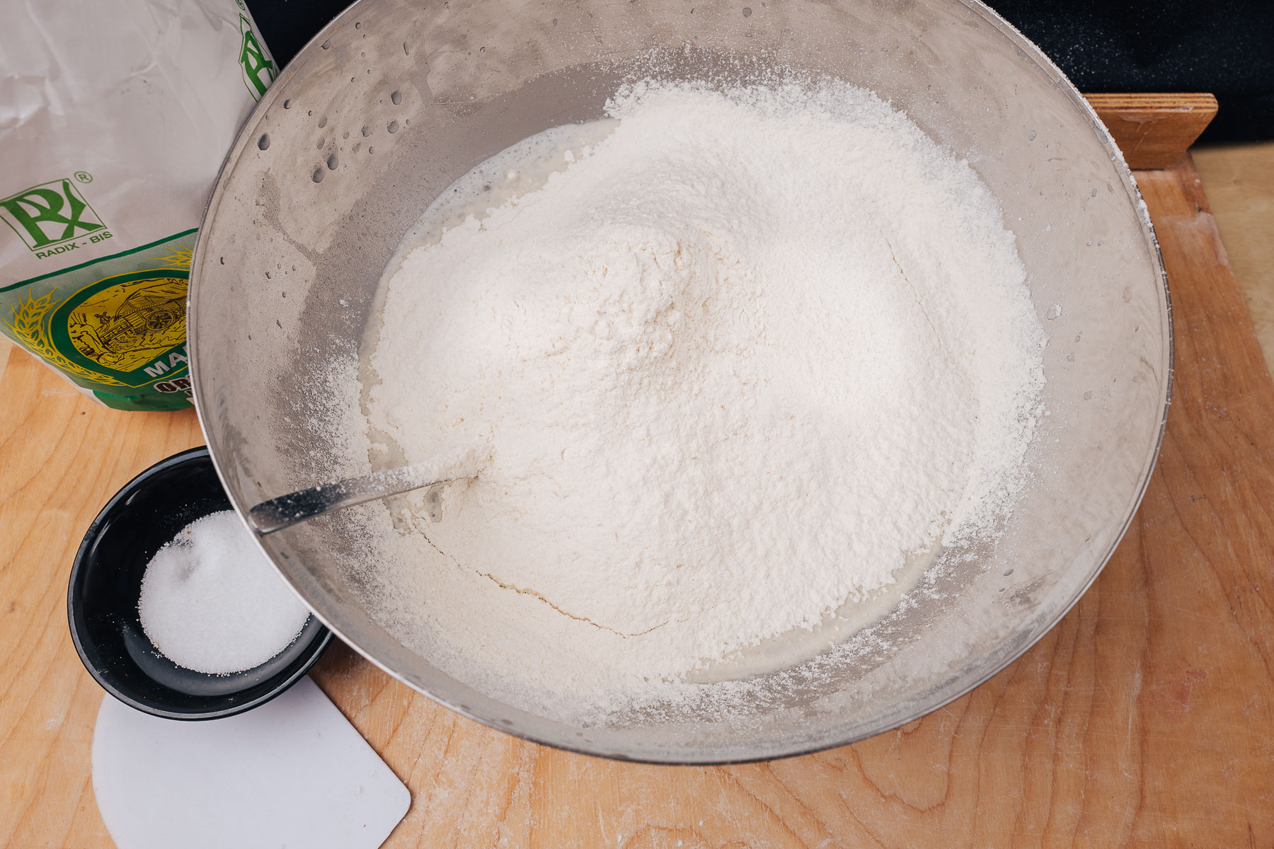 Wsyp do miski z wodą i zakwasem około połowy przygotowanej mąki i zacznij mieszać.
